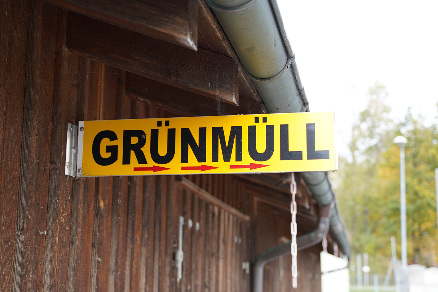 Ein hellgrünes Schild mit dem Aufdruck Grünmüll und drei roten Pfeilen, die nach rechts zeigen