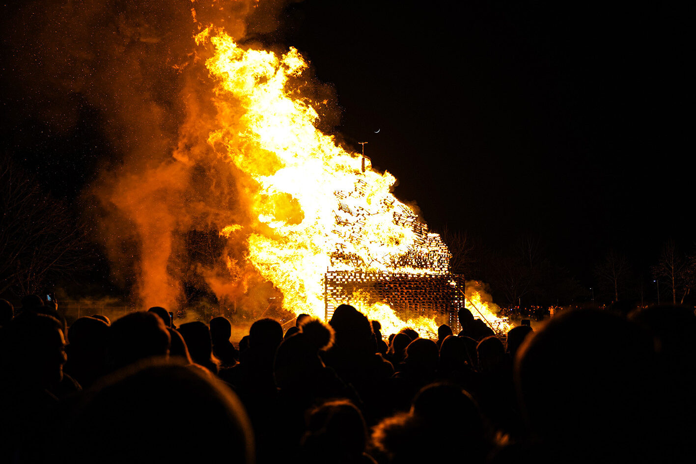 Blick bei Dunkelheit über die Köpfe von vielen Zuschauerinnen und Zuschauern hinweg zu einem brennenden Funken