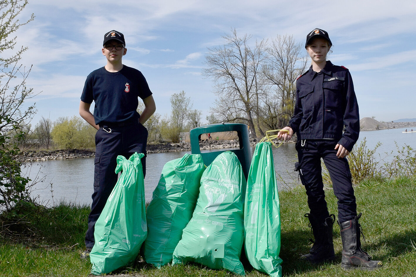 Auf einer Wiese stehen zwei Mitglieder der Feuerwehrjugend Hard mit vier gefüllten Müllsäcken