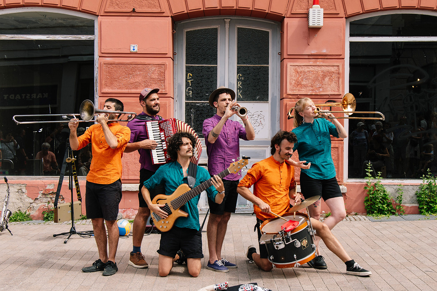 Fünf Musiker und eine Musikerin der Band Desmadre Orkesta spielen vor einem Gebäude auf ihren Instrumenten