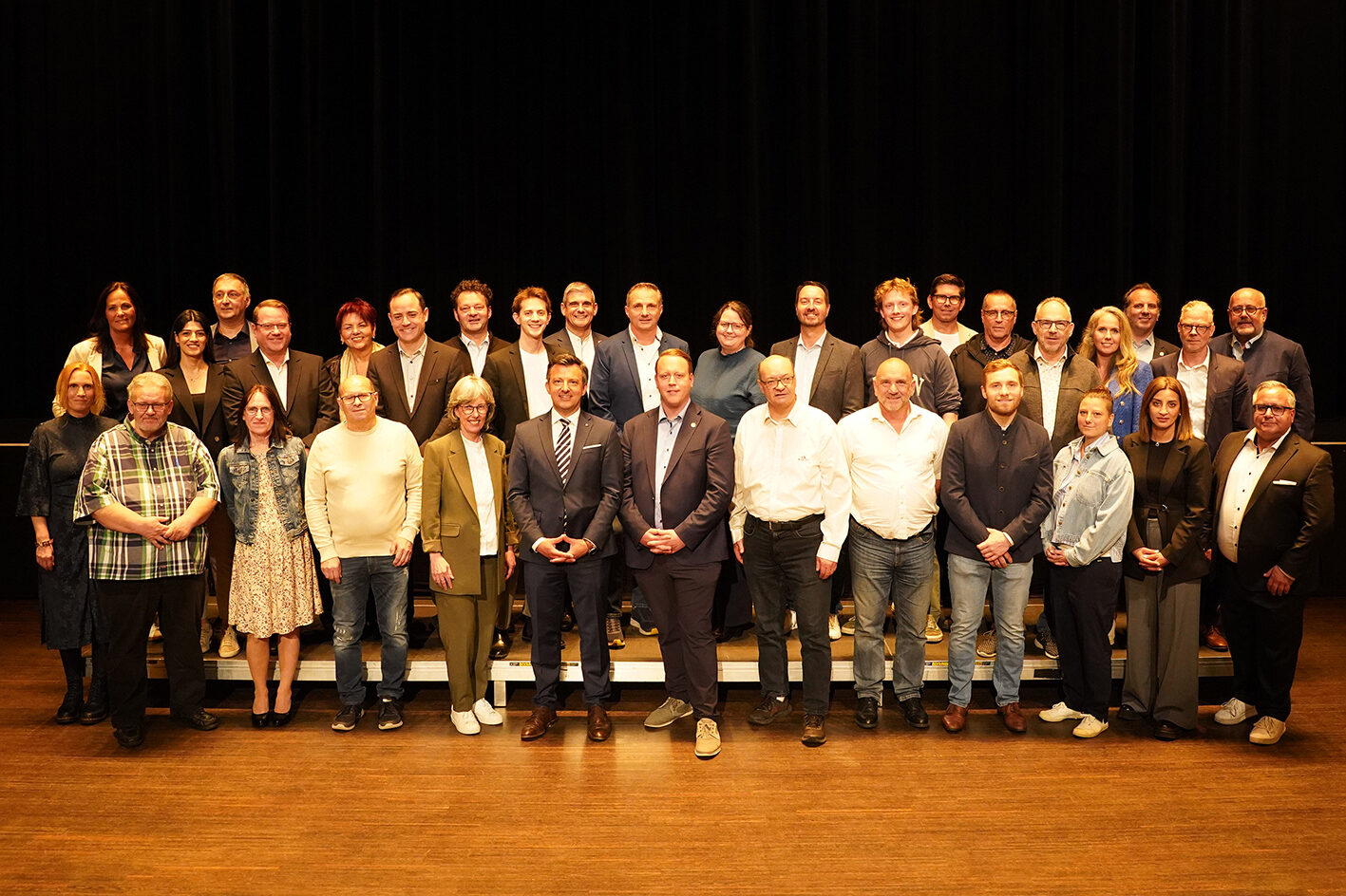 Gruppenbild mit den Harder Gemeindevertreterinnen und Gemeindevertretern, die vor einem schwarzen Vorhang in die Kamera lächeln