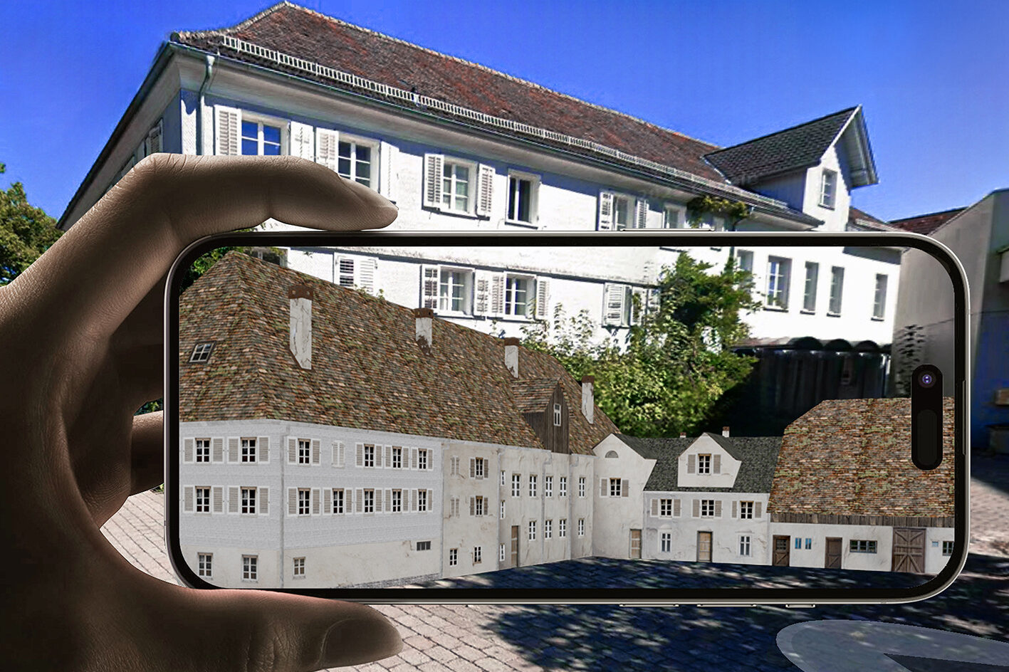 Eine Hand hält ein Smartphone quer. Auf dem Bildschirm ist zu sehen, wie ein Gebäudekomplex in früherer Zeit ausgesehen hat. Hinter dem Smartphone ist das Gebäude zu sehen, wie es in der Gegenwart aussieht
