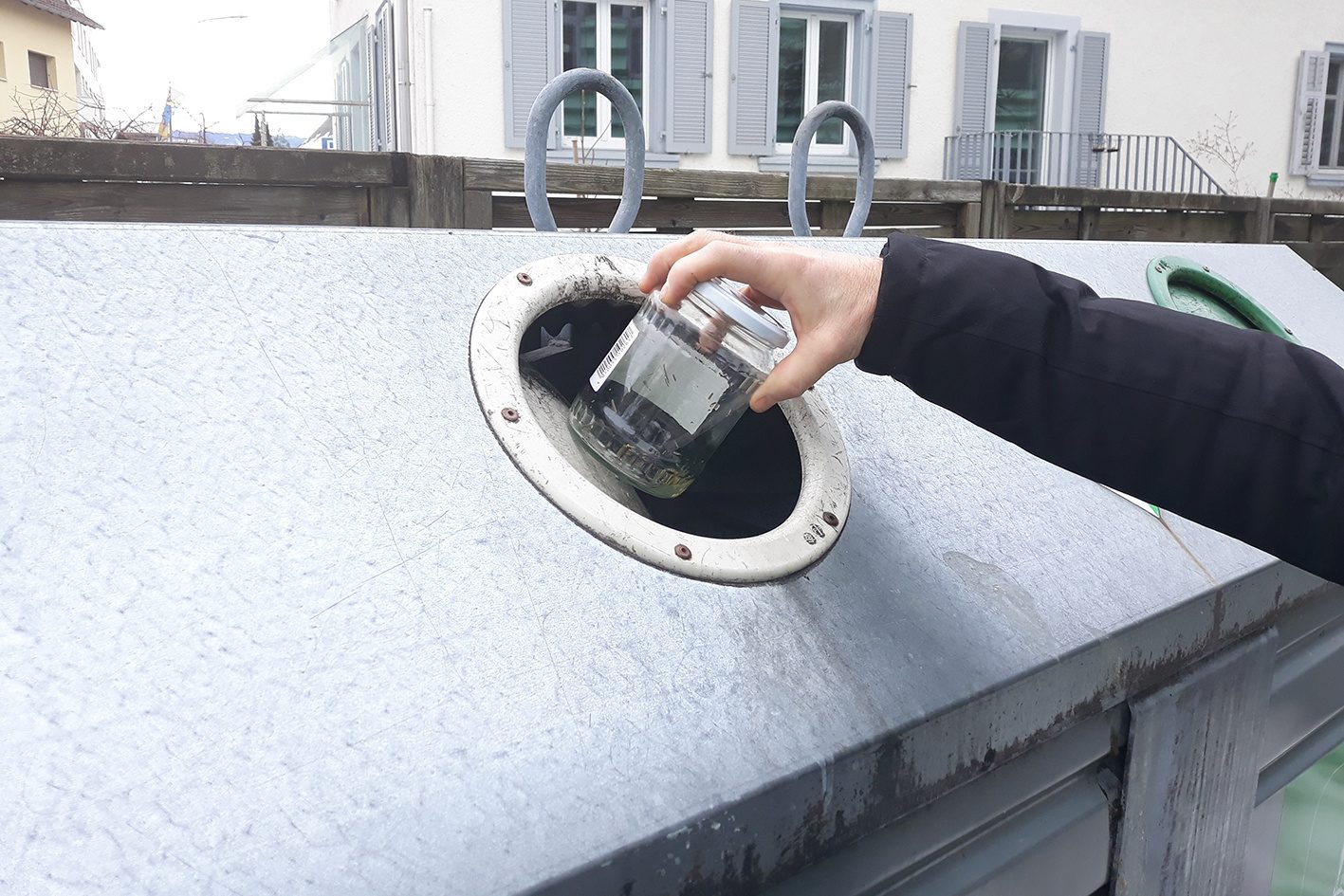 Eine Person, von der man nur den rechten Arm sieht, wirft Altglas in einen Sammelcontainer