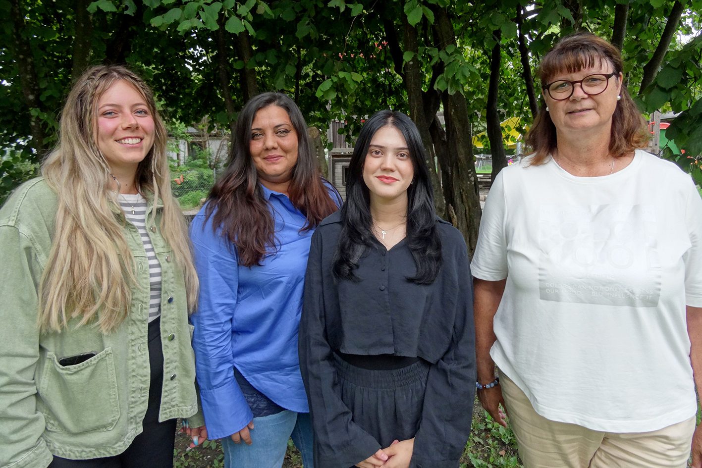 Vier Kindergärtnerinnen stehen lächelnd vor einem Baum