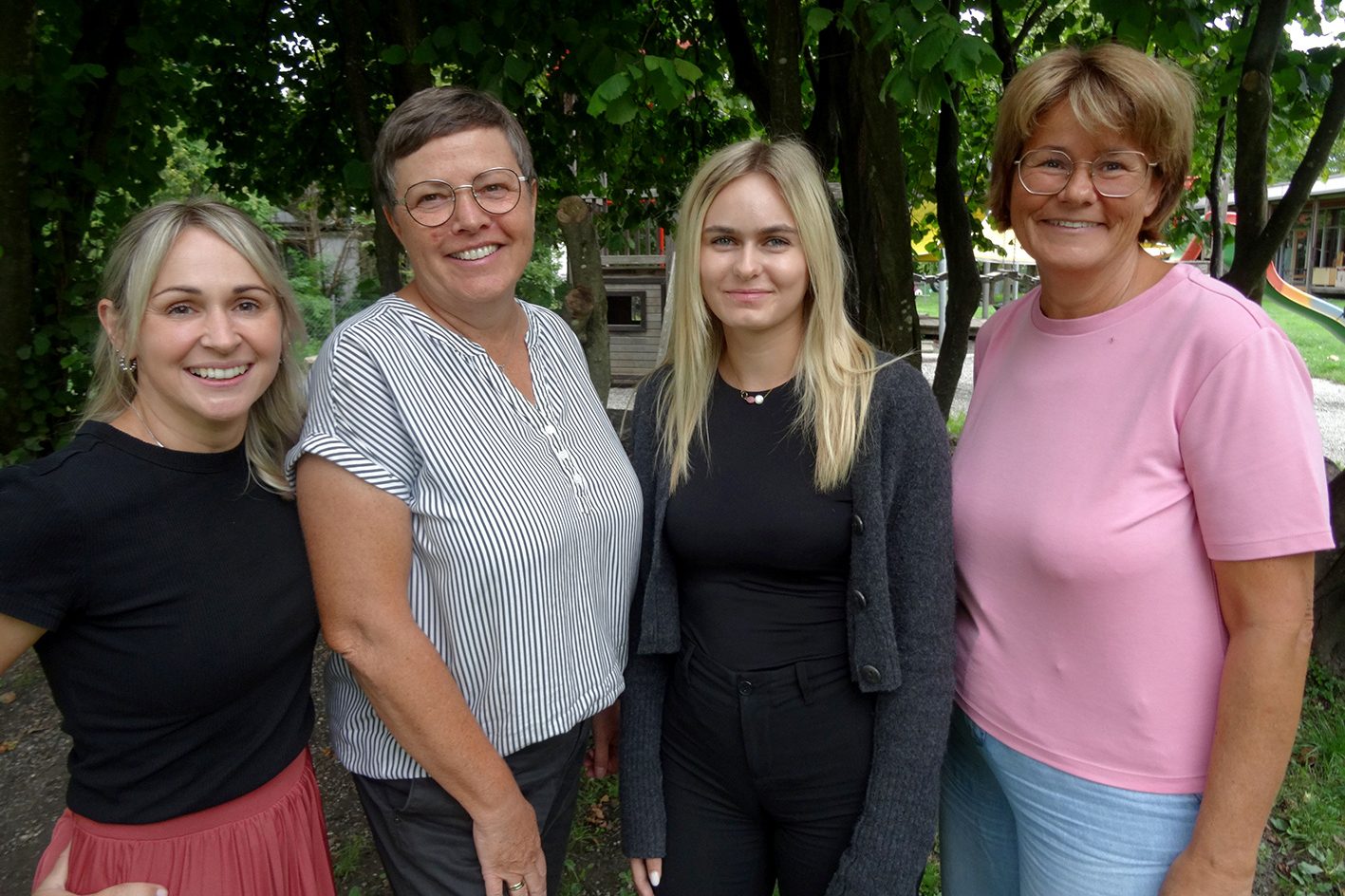Vier Kindergärtnerinnen stehen lächelnd vor einem Baum.