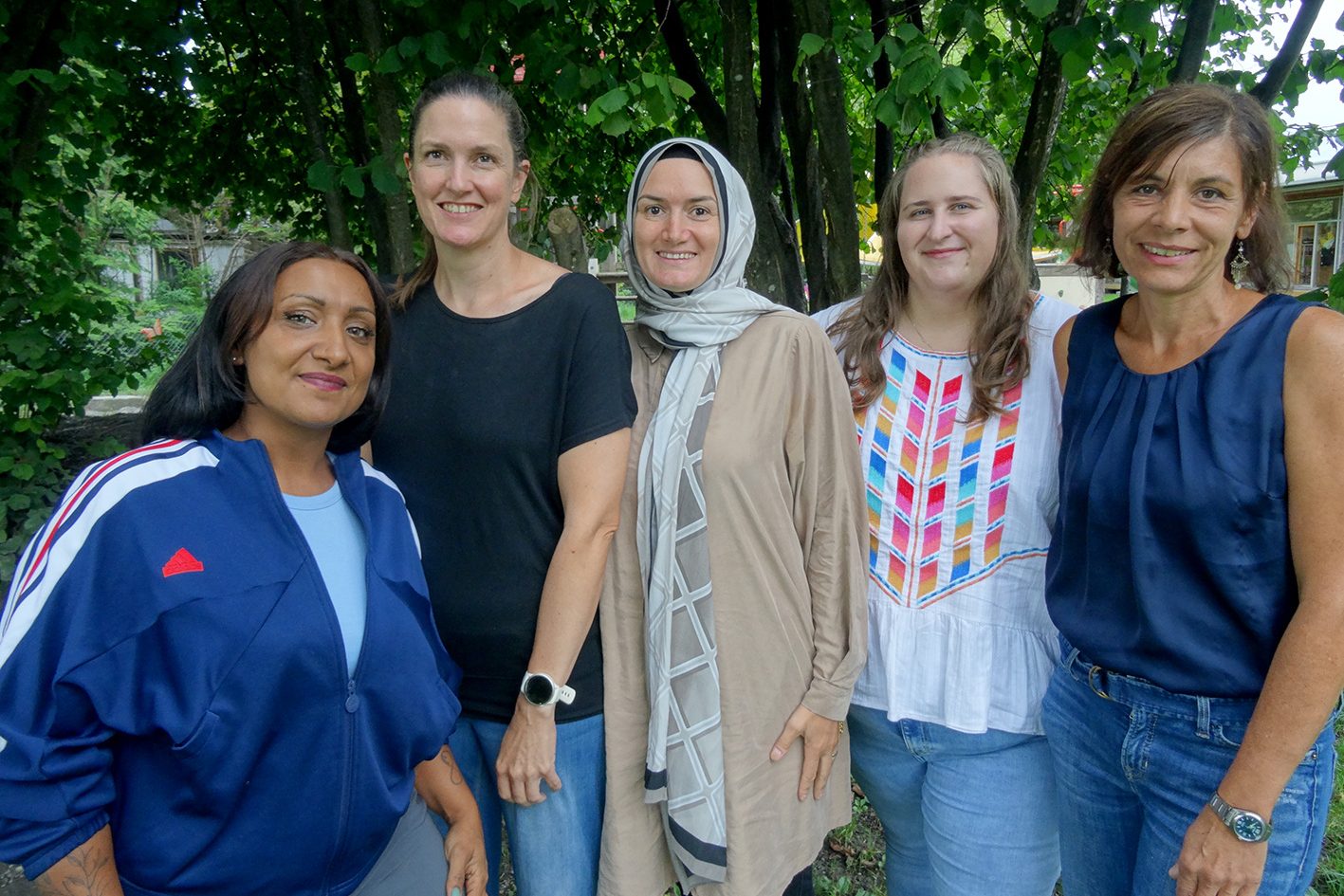 Fünf Kindergärtnerinnen stehen lächelnd vor einem Baum.