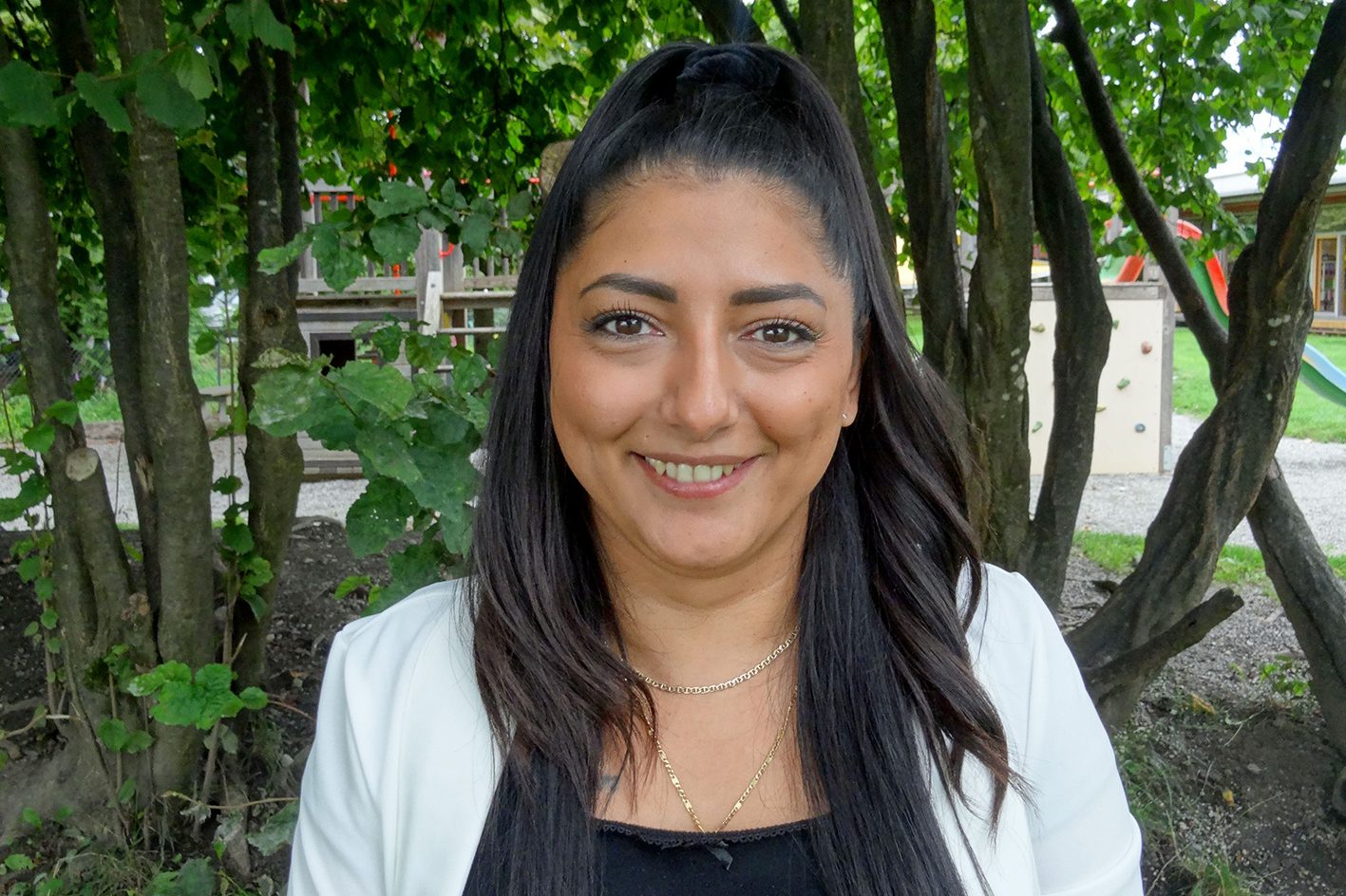 Eine Kindergärtnerin steht lächelnd vor einem Baum.