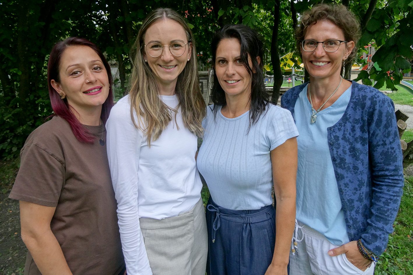 Vier Kindergärtnerinnen stehen lächelnd vor einem Baum.