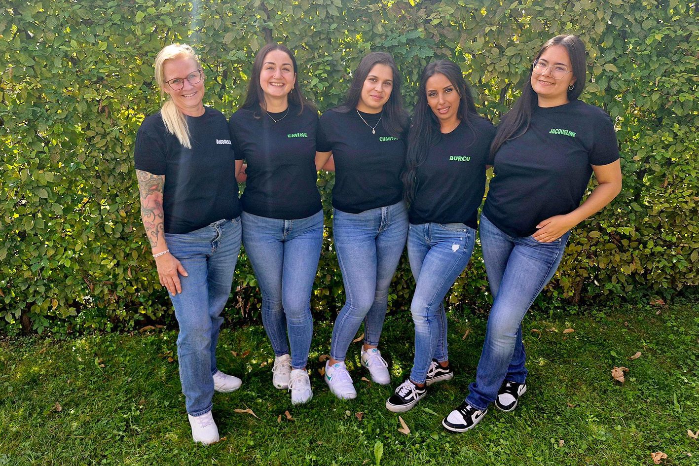 Fünf Kleinkindbetreuerinnen stehen lächelnd auf dem Rasen vor einer Hecke.