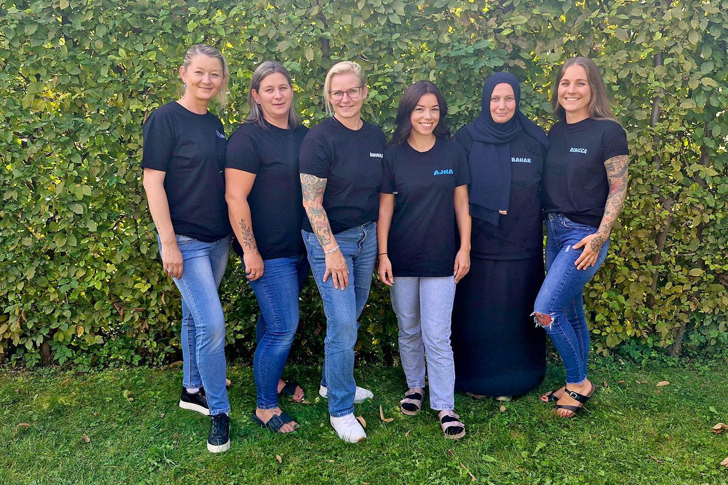 Sechs Kleinkindetreuerinnen stehen lächelnd auf dem Rasen vor einer Hecke.