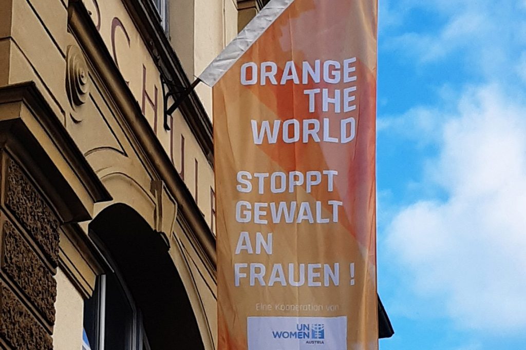 Eine orange Fahne mit der Aufschrift Orange the World, stoppt Gewalt an Frauen hängt an der Fassade einer Schule