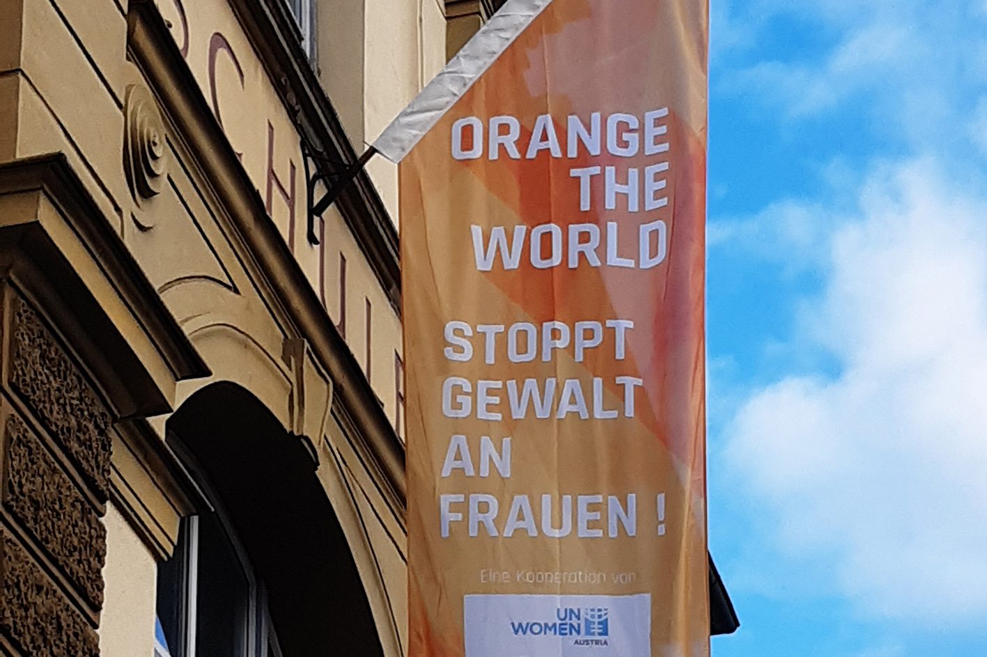 Eine orange Fahne mit der Aufschrift Orange the World, stoppt Gewalt an Frauen hängt an der Fassade einer Schule