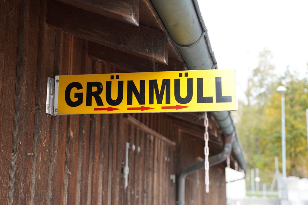 Ein hellgrünes Schild mit dem Aufdruck Grünmüll und drei roten Pfeilen, die nach rechts zeigen