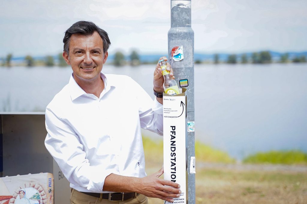 Bürgermeister Martin Staudinger wirft eine Flasche in eine Pfandstation und lächelt in die Kamera.