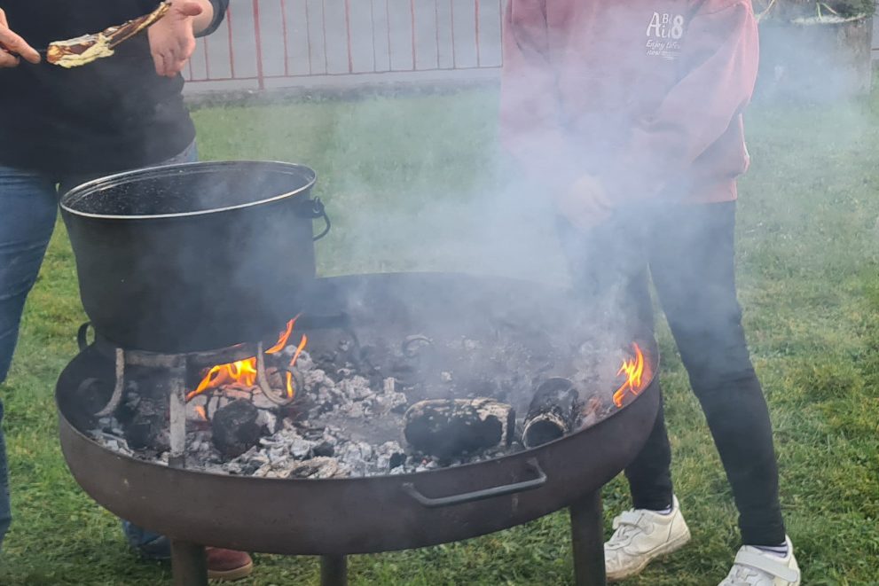 Jugendliche stehen an einer feuerschale und kochen etwas in einem Topf