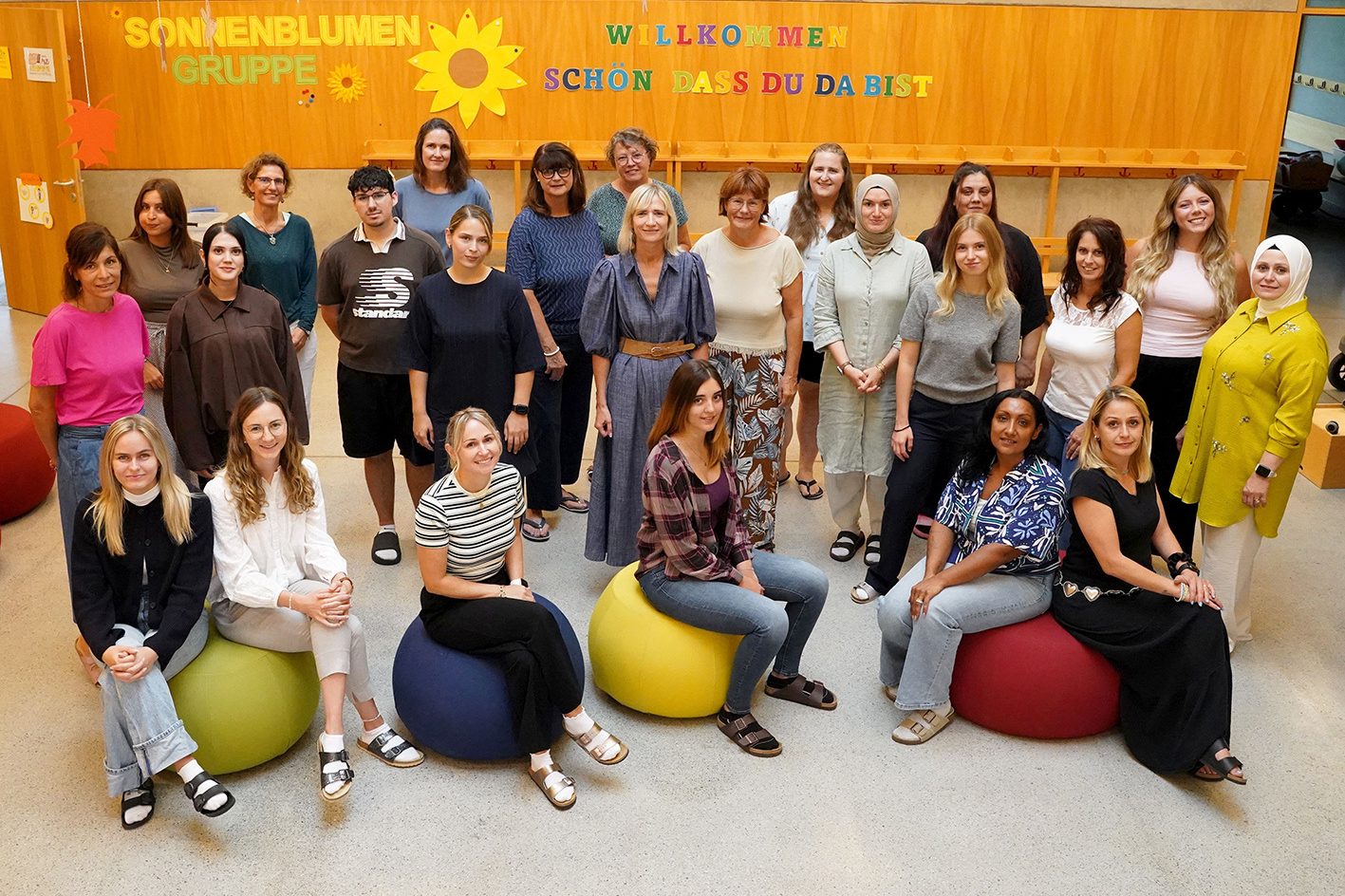 Gruppenfoto des Teams vom Kindergarten Falkenweg vor der Wand der Sonnenblumen-Gruppe.